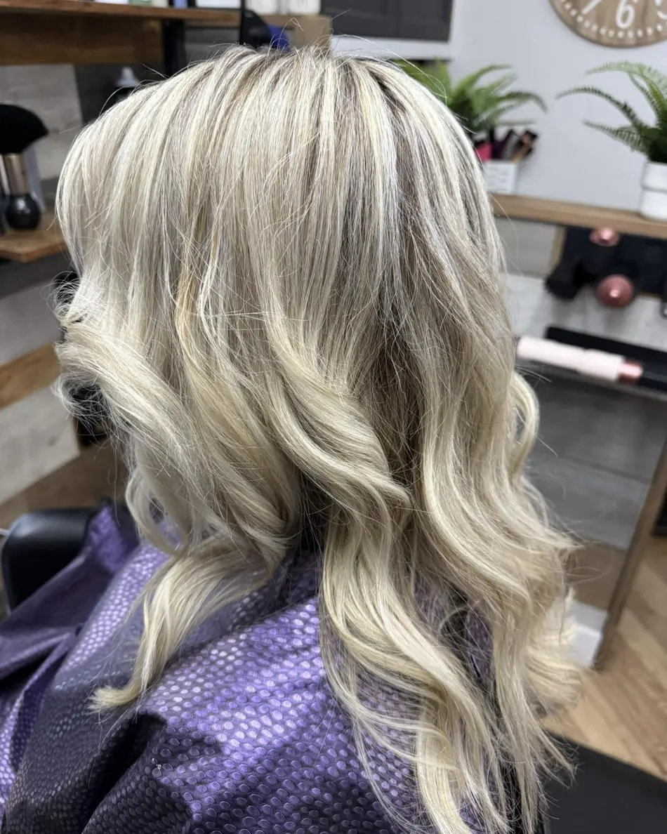 Platinum blonde waves over a purple salon cape, back view